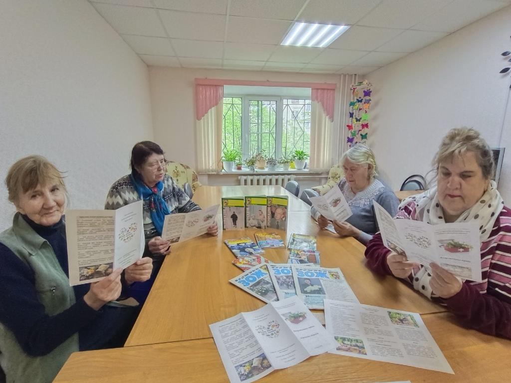 За столами сидят получатели социальных услуг 4 человека. На столах лежат журналы о здоровье. В руках женщины держат буклеты "Лекарственные травы - источник здоровья"