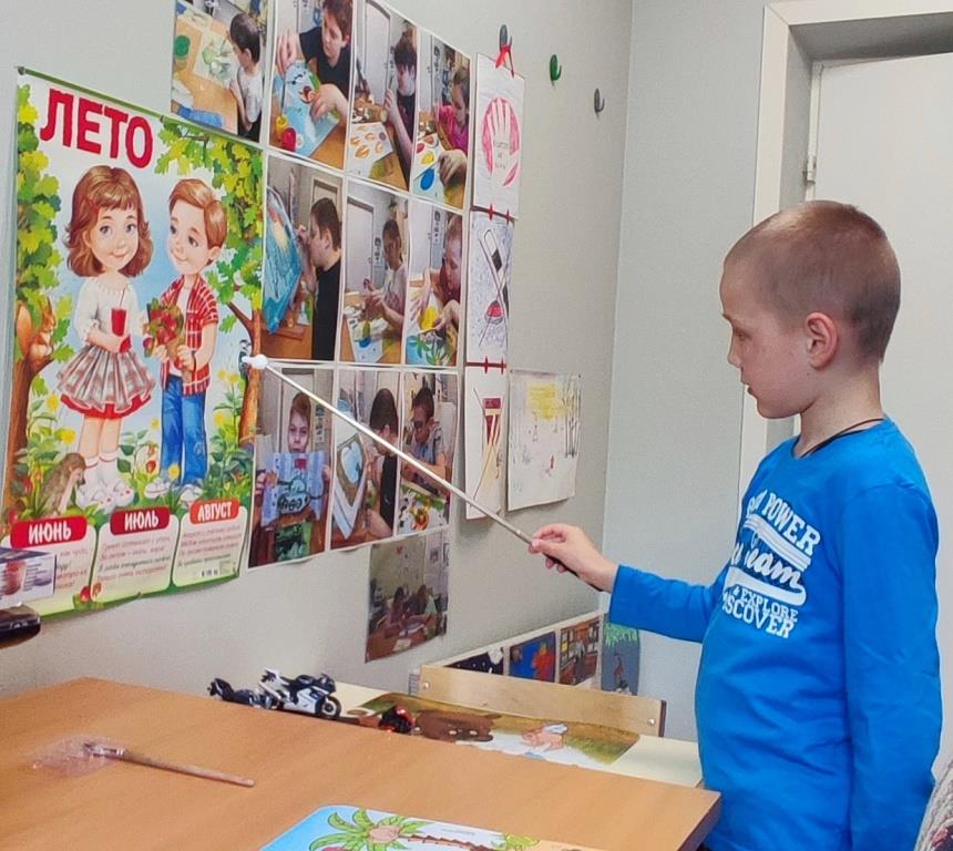 Девочка за столом из красного листа бумаги с помощью фигурного дырокола делает шарики для аппликации.